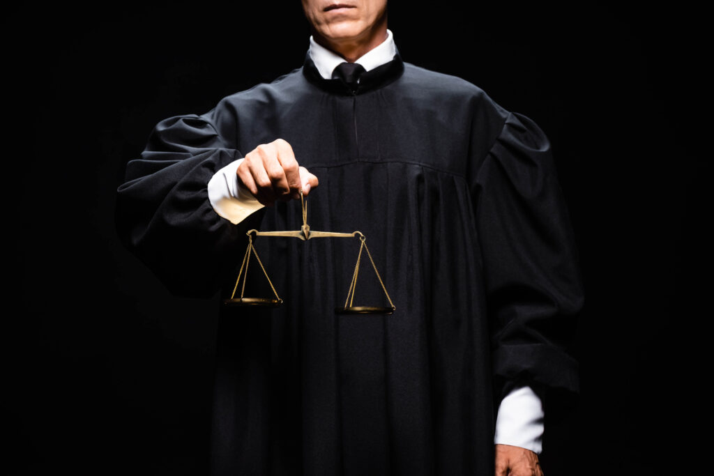 cropped view of judge in judicial robe holding scales of justice isolated on black