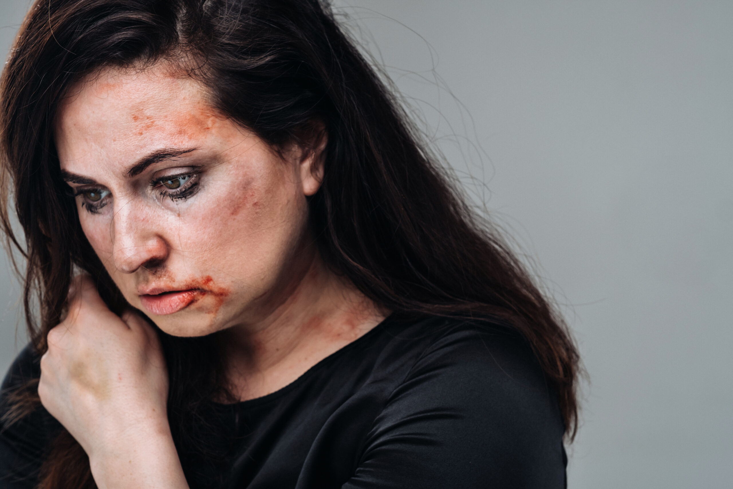 a battered woman in black clothes on an isolated gray background. Violence against women