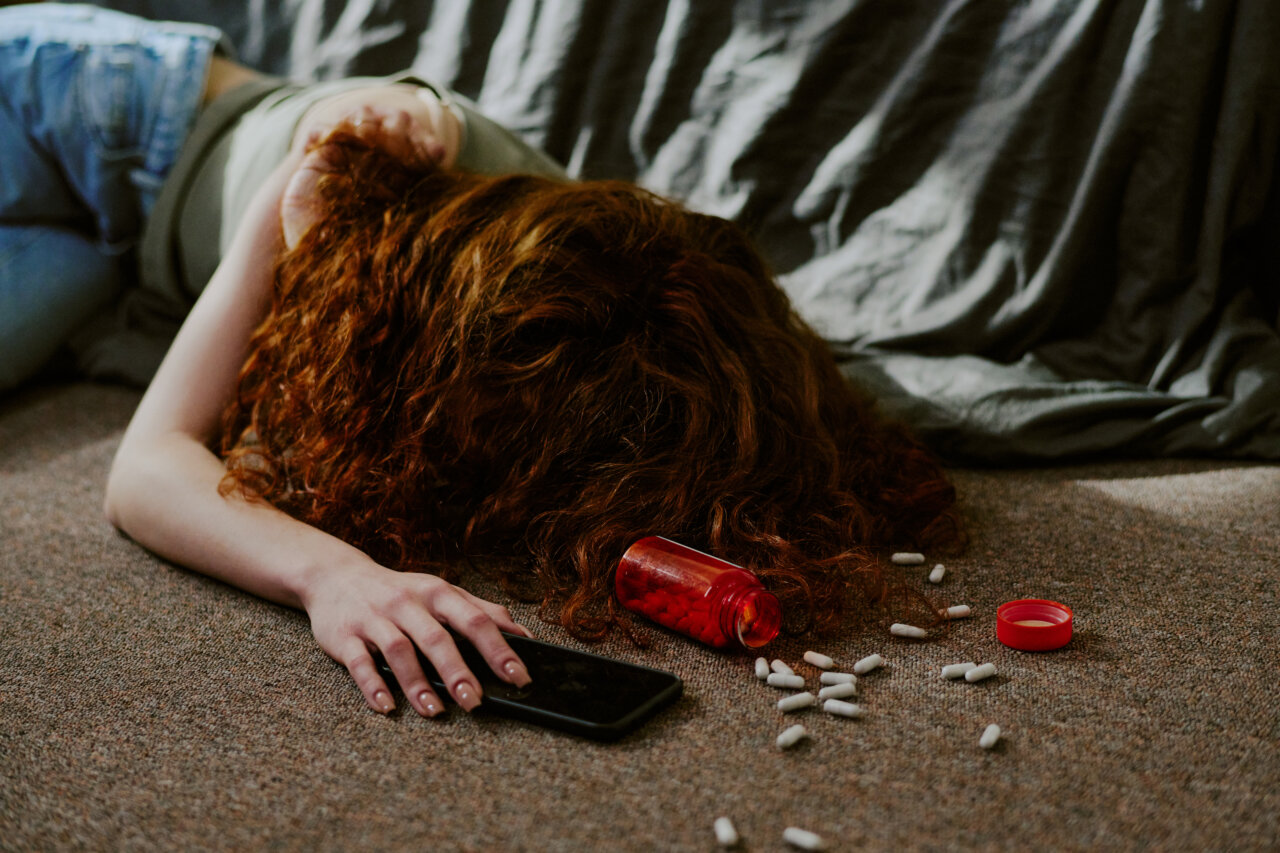 Mujer joven con cabello rizado sobre una alfombra con pastillas esparcidas.