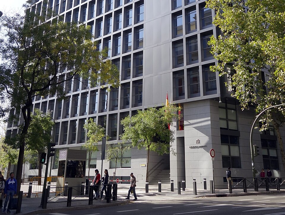 Edificio de la Audiencia Nacional en Madrid con árboles y personas caminando