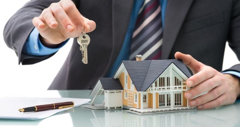 Hombre sosteniendo llaves frente a una casa en miniatura