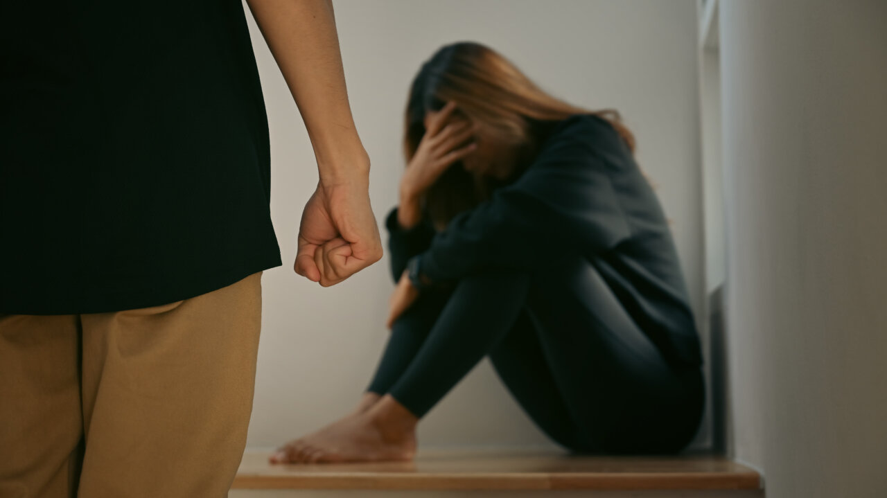 Mujer angustiada sentada mientras un hombre la amenaza.
